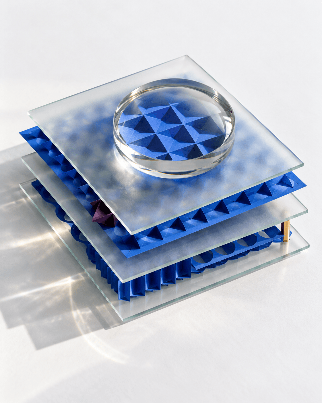 Plaques de verre dépoli superposées sur des couches de papier bleu découpé, une lentille grossit leur structure.