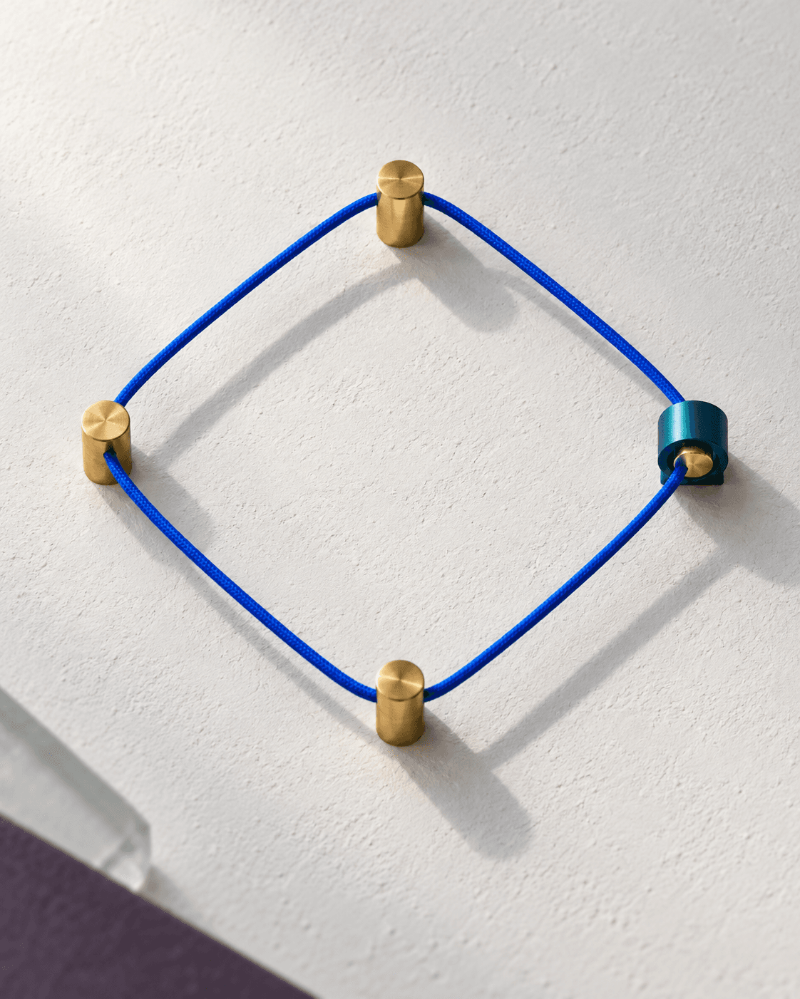 Fil bleu tendu en boucle fermée entre quatre tiges de laiton, dont une pince teal marque le point de contrôle.